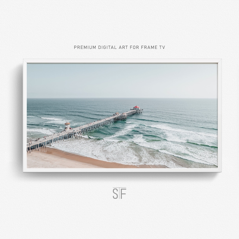 May include: An aerial view of a pier extending out into the ocean with white capped waves crashing on the sandy beach. The pier has a red roof at the end.