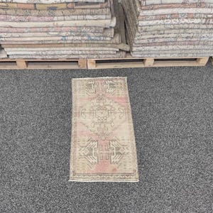 May include: A rectangular area rug featuring a faded pink and beige color palette with intricate geometric patterns and symmetrical motifs. The rug has a central diamond shape and decorative borders, showcasing a weathered, low-pile texture.