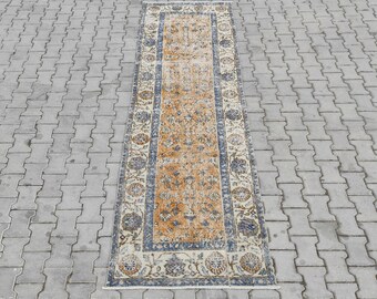 May include: A rectangular, distressed-look rug with an intricate floral pattern. The rug features a central field of warm orange tones, framed by a border of blue and cream floral designs. The rug is placed on a gray, textured surface.