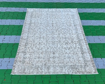 May include: A vintage cream-coloured rug with a floral pattern in a darker shade of brown. The rug is laid out on a green and grey tiled surface.