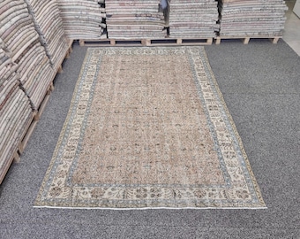 May include: A rectangular area rug featuring a central field of muted tan and beige tones with intricate floral and vine patterns in shades of blue, brown, and cream. The rug is framed by a wide, detailed border with repeating botanical motifs.