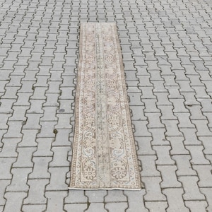 Pode incluir: Um tapete corredor longo e bege com um padrão floral tradicional. O tapete tem uma borda marrom claro e um design central com um motivo repetitivo.