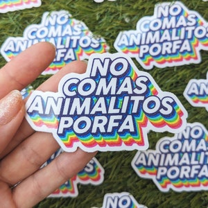以下が含まれることがあります： 「No comas animalitos porfa」と書かれた虹色のステッカーのクローズアップ。ステッカーは緑の芝生の上に置かれています。