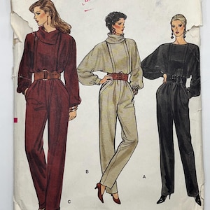 May include: A Vogue Patterns sewing pattern envelope for size 8, featuring illustrations of three jumpsuits with high collars, long sleeves, and wide belts. The text includes "Vogue Patterns", "Taille Size 8", "Pattern/Patron", and "No Refund Fabric Ville".