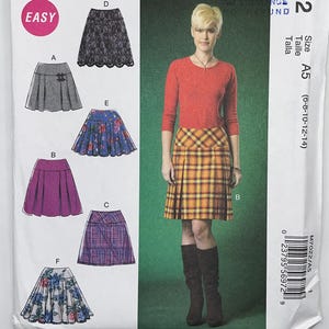 May include: McCall's M7022 sewing pattern envelope for skirts in sizes 6-8-10-12-14. The front displays illustrations of six skirt variations labeled A through F, including lace, plaid, and floral designs, alongside a photo of a plaid skirt.