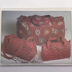 May include: Three quilted bags in a red floral pattern. The largest bag has a drawstring closure and two handles. The other two bags are smaller, with handles and a similar floral design. The bags are arranged on a white background.