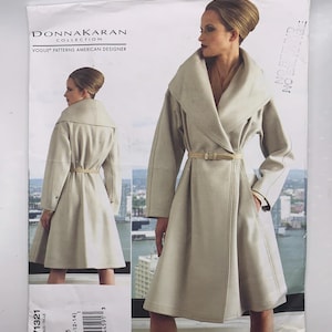 May include: A sewing pattern for a Donna Karan Collection coat, V1321. The image shows a model wearing a light beige coat with a wide collar and belt. The Vogue Patterns American Designer logo is visible.