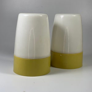 May include: Two white ceramic salt and pepper shakers with yellow bases. The shakers are round and have a smooth, glossy finish.