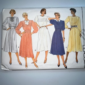 Op de afbeelding: Vintage naaipatroon met illustraties van vijf verschillende jurken. De jurken zijn in verschillende kleuren, waaronder wit, koraal, blauw en geel. Elke jurk heeft een uniek ontwerp, met details zoals strikken, plooien en riemen.