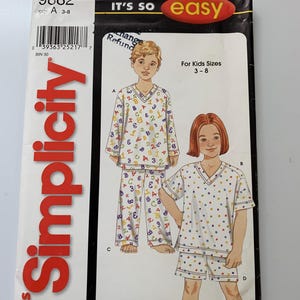 Puede incluir: Patrón de costura Simplicity número 9882 para niños de tallas 3-8. El patrón incluye instrucciones para hacer una camiseta de pijama de manga larga con cuello en V y pantalones, y una camiseta de pijama de manga corta con pantalones cortos. El patrón está impreso en papel blanco con texto negro y rojo.