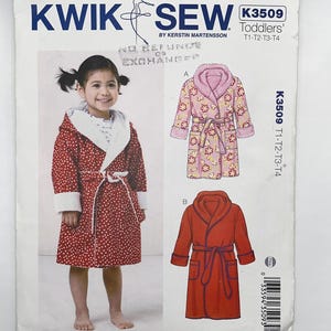 May include: A Kwik Sew K3509 sewing pattern envelope for toddlers' robes. The front displays a red robe with white polka dots and a white collar, alongside illustrations of a floral print robe and a solid red robe, each with a tie belt and pockets.