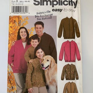 Op de afbeelding: Simplicity naaipatroon nummer 5477, gemakkelijk te naaien, Fabricville, Geen ruil, Geen restitutie. Het patroon bevat instructies voor het maken van een ritsjack met een geribbelde kraag en manchetten. Het patroon wordt getoond op een gezin van drie en een hond, die de jas in verschillende kleuren en patronen dragen.