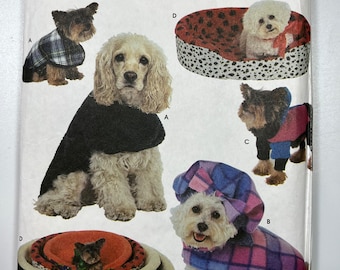 May include: A Simplicity Crafts sewing pattern for making dog beds and clothes. The pattern includes instructions for making a plaid dog coat, a hooded cape, a dog bed with a black and white patterned fabric, and a dog bed with a red and white patterned fabric. The pattern also includes instructions for making a dog bed with a black and white patterned fabric.