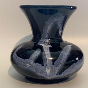 Puede incluir: Un pequeño jarrón de cerámica negro con un diseño de esmalte blanco. El jarrón tiene una base ancha y redonda y un cuello estrecho.