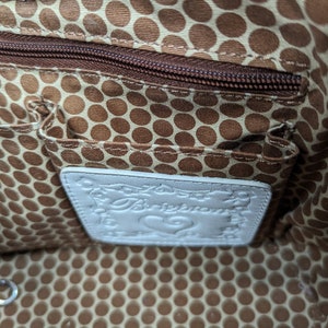 May include: Interior of a handbag with a brown polka dot lining and a zippered pocket. A white leather tag with the brand name "Brighton" is visible. The bag's interior also features small pockets.