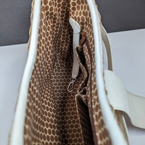 May include: A woven tote bag with a white leather trim and handles. The interior features a brown fabric with a repeating dot pattern. A small zippered pocket and a silver-colored clasp are visible inside the bag.