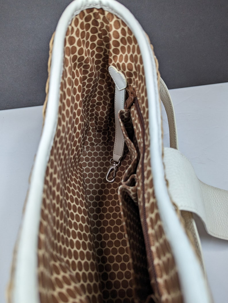 May include: A woven tote bag with a white leather trim and handles. The interior features a brown fabric with a repeating dot pattern. A small zippered pocket and a silver-colored clasp are visible inside the bag.