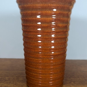 May include: A tall, brown ceramic vase with a textured, ribbed design. The vase has a slightly flared top and a glossy finish. The color is a warm, earthy tone, suitable for home decor.