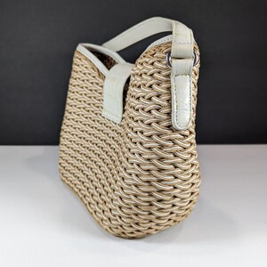 May include: A woven handbag with a beige and white pattern. The bag has a rounded shape and a white leather handle and trim. The bag is made of a thick, textured material and has a clean, modern design.