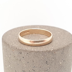 May include: A smooth, polished rose gold band ring with a rounded profile. The metal surface reflects light evenly across its circumference, showcasing a simple, continuous circular design without any gemstones or additional decorative elements.