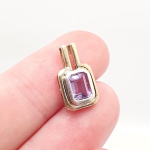 May include: A rectangular pendant with a light purple gemstone set in a gold and silver frame. The pendant has a rectangular bail at the top for a chain. The gemstone is a light purple color.