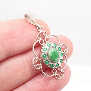 May include: A silver pendant with a floral design. The pendant features a central oval of green enamel surrounded by small green enamel dots. The pendant has a decorative, openwork design with a loop for a chain.