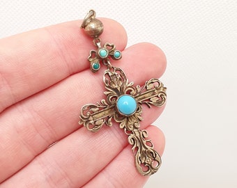 May include: A silver pendant with a turquoise cross and smaller turquoise stones. The cross is ornate and has a detailed design.