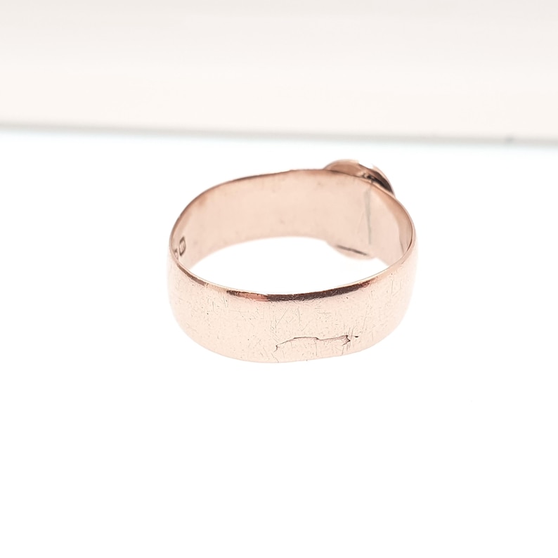 May include: A rose gold ring with a simple band design. The ring has a smooth, polished surface with a slight crack visible on the band. The ring is set against a white background.
