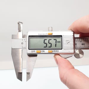 May include: A digital caliper showing a measurement of 5.57 mm. The silver caliper has a digital display. The device is held by a person's hand. The measurement is approximately 0.22 inches.