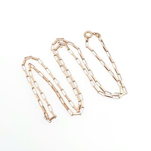 May include: A rose gold chain necklace featuring elongated rectangular links connected in a repeating pattern. The necklace includes a circular spring ring clasp at one end, showcasing a metallic finish and a delicate, uniform construction throughout.