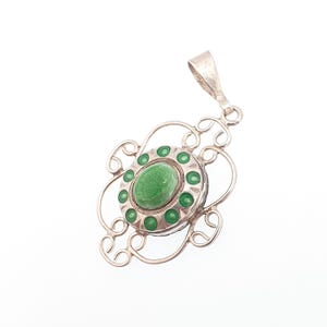 May include: A silver pendant with an oval, light green center stone surrounded by smaller green stones. The pendant has a decorative, openwork design with a loop at the top for a chain. The pendant is set against a white background.