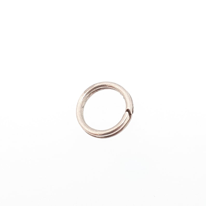 May include: A small, silver-coloured split ring, designed to hold keys or other small items. The ring is circular with a split, allowing items to be added or removed. The metal has a slightly worn appearance, suggesting it is made of a durable material.