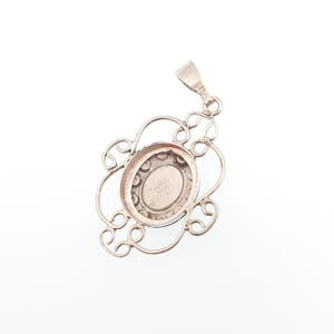 May include: A silver pendant with an oval center and an ornate, openwork design. The pendant has a bail for attaching to a chain and is set against a white background. The design features a floral-like pattern.
