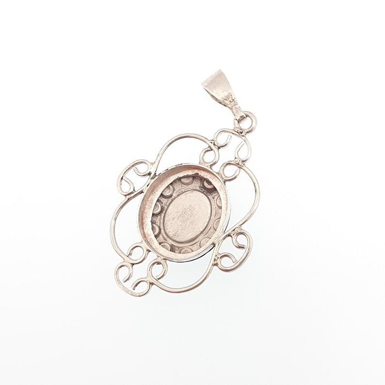 May include: A silver pendant with an oval center and an ornate, openwork design. The pendant has a bail for attaching to a chain and is set against a white background. The design features a floral-like pattern.