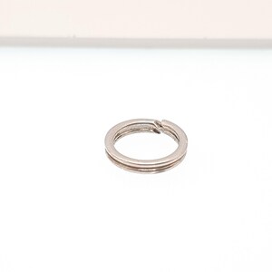 May include: A small, silver split key ring. The key ring is circular with a split for adding keys. The key ring is made of metal and has a shiny finish. A common item for organizing keys.