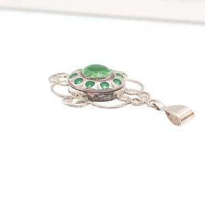 May include: A silver pendant with a central green stone and green enamel accents. The pendant has an ornate, openwork design with a bail for a chain. The piece is likely vintage or antique.