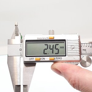 May include: A digital caliper displaying a measurement of 2.45 mm, or approximately 0.096 inches. The caliper is silver with a digital display and buttons labeled "OFF", "ON", and "ZERO". The image shows a close-up of the tool.