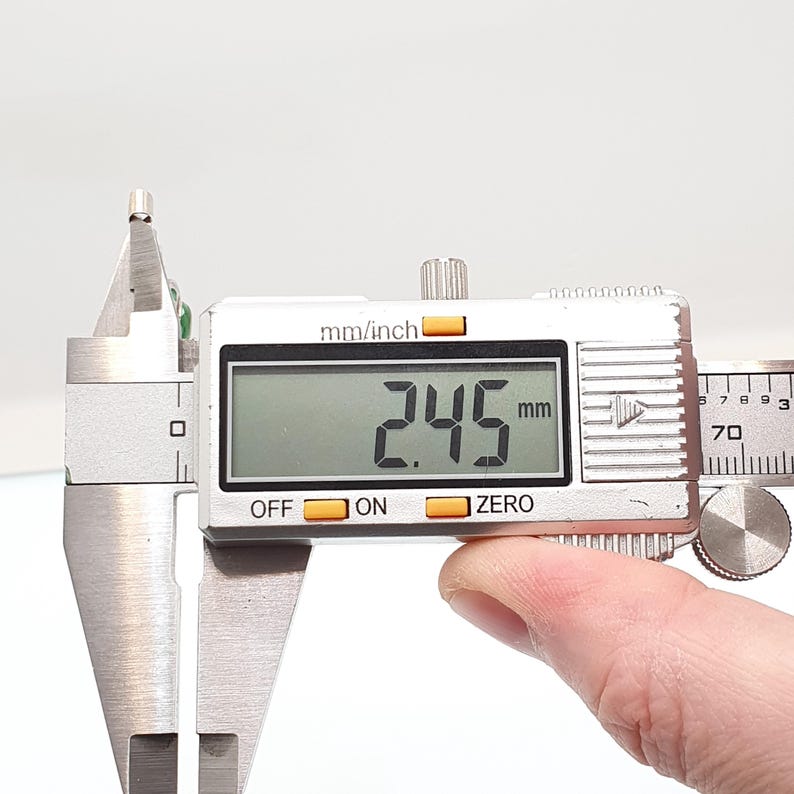 May include: A digital caliper displaying a measurement of 2.45 mm, or approximately 0.096 inches. The caliper is silver with a digital display and buttons labeled "OFF", "ON", and "ZERO". The image shows a close-up of the tool.