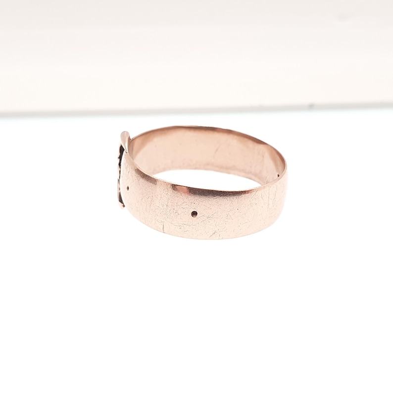 May include: A rose gold ring with a textured surface. The ring has a small decorative element and two small holes. The ring is shown on a white background.