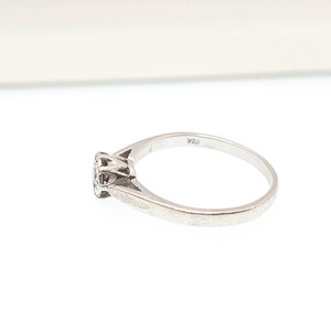 Puede incluir: Un anillo de plata con un peque&ntilde;o engaste redondo de diamantes. La banda del anillo es fina y lisa, con una inscripci&oacute;n sutil. El anillo se muestra sobre un fondo blanco, resaltando su elegancia.