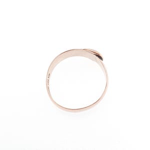 May include: A rose gold ring with a minimalist design. The ring features a smooth, curved band that wraps around to form a small, raised detail at the top. The ring is set against a white background.