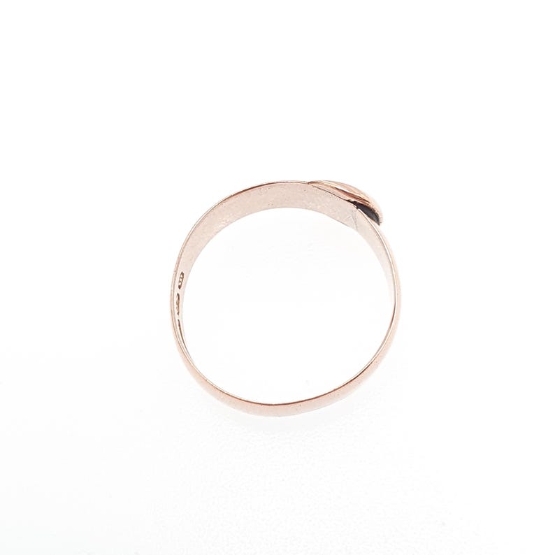 May include: A rose gold ring with a minimalist design. The ring features a smooth, curved band that wraps around to form a small, raised detail at the top. The ring is set against a white background.