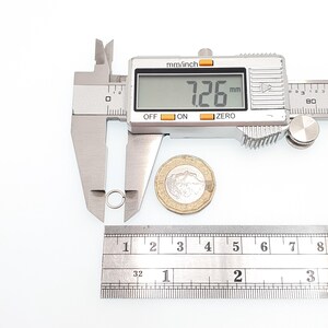 May include: A silver jump ring is measured with a digital caliper, displaying 7.26 mm. A ruler shows inches and a coin is next to the ring. The caliper reads "mm/inch", "OFF", "ON", and "ZERO".