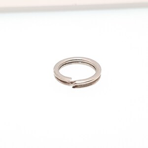 May include: A small, silver-coloured split ring, designed for attaching keys or other small items. The ring is circular with a split opening for easy attachment. The metal has a shiny finish, reflecting the light.