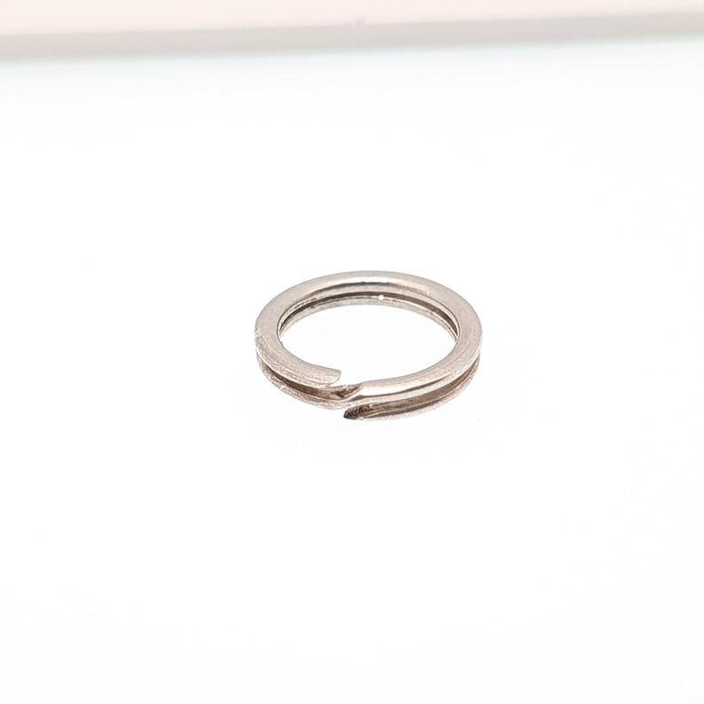 May include: A small, silver-coloured split ring, designed for attaching keys or other small items. The ring is circular with a split opening for easy attachment. The metal has a shiny finish, reflecting the light.