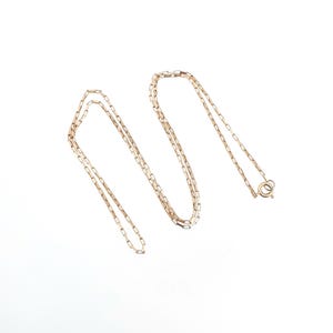 Puede incluir: Un collar de cadena de oro rosa que presenta una serie de pequeños eslabones rectangulares y alargados conectados en un patrón continuo. El collar incluye un cierre de resorte circular en un extremo, lo que proporciona un cierre seguro.