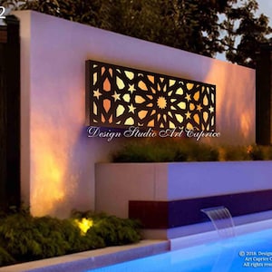 May include: A rectangular black metal wall panel featuring an intricate geometric star pattern with warm backlighting. The panel is mounted on a white wall above a pool, with the text Design Studio Art Caprice visible below the panel.
