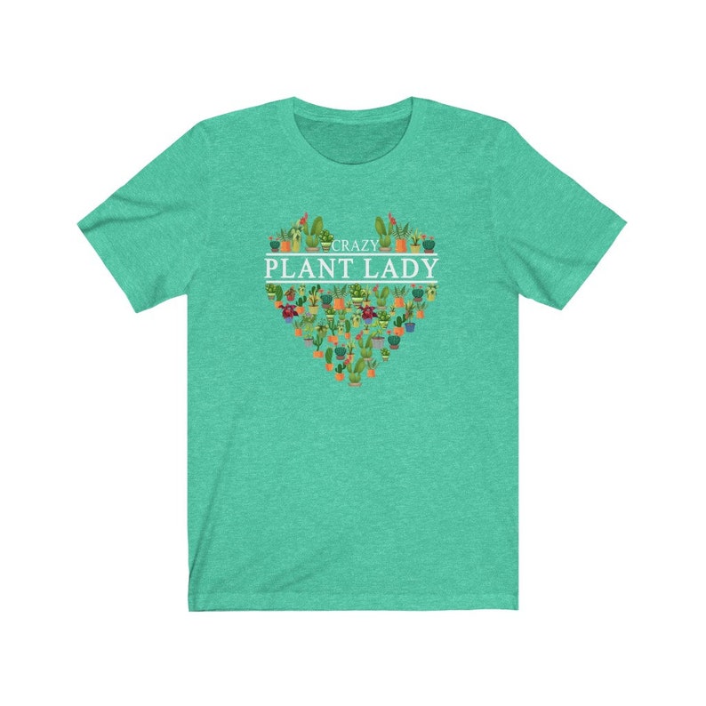 Puede incluir: Una camiseta verde turquesa con un dise&ntilde;o en forma de coraz&oacute;n blanco con el texto "Crazy Plant Lady" rodeado de una variedad de plantas en macetas.