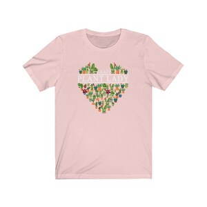 Puede incluir: Camiseta rosa de manga corta con un dise&ntilde;o blanco en forma de coraz&oacute;n que presenta una variedad de plantas en macetas y el texto "Crazy Plant Lady".