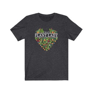 Puede incluir: Una camiseta gris oscuro jaspeada con un dise&ntilde;o en forma de coraz&oacute;n que presenta una variedad de plantas en macetas. El texto "Crazy Plant Lady" est&aacute; impreso en blanco sobre el coraz&oacute;n.